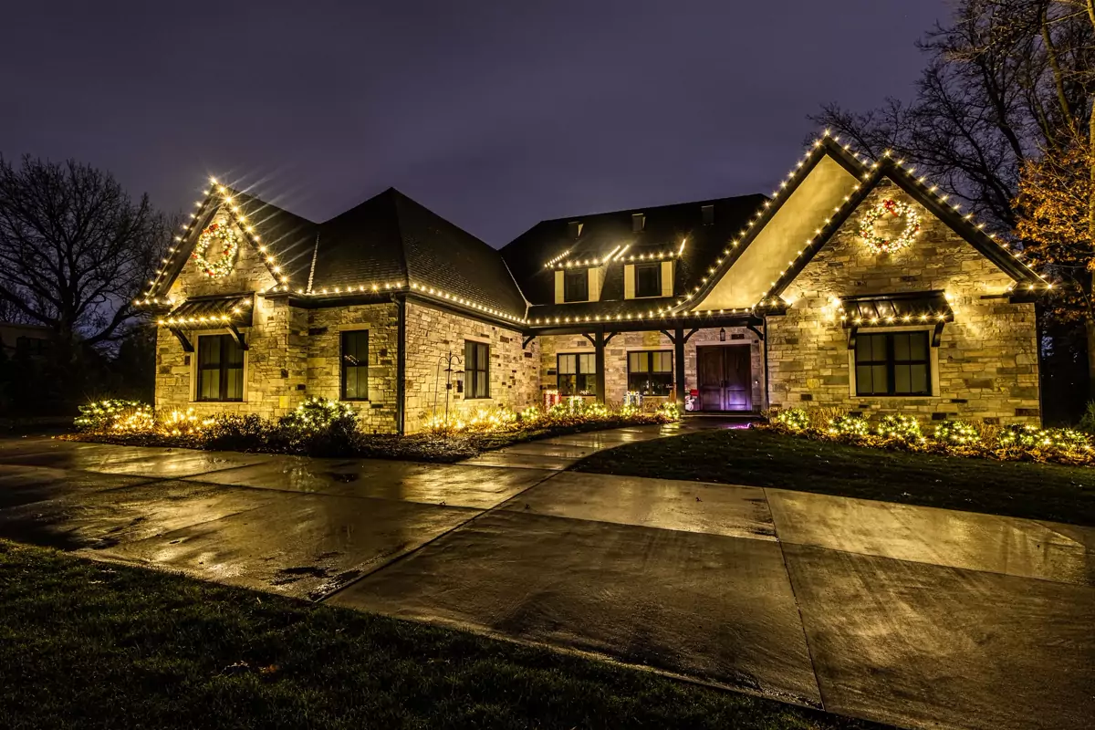 Stone home outlined in warm white C9 lights with lit wreaths on both gables